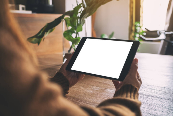 Mockup image of hands holding and using black tablet pc with blank white desktop screen on wooden table - Photo, Image