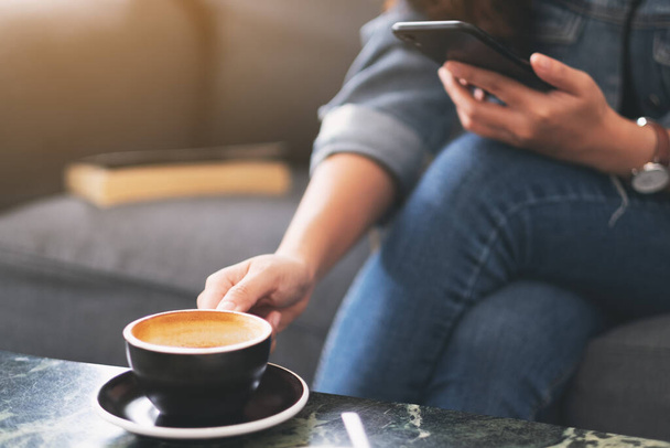Imagen de cerca de una mujer sosteniendo y usando el teléfono móvil mientras bebe café en la cafetería
 - Foto, Imagen