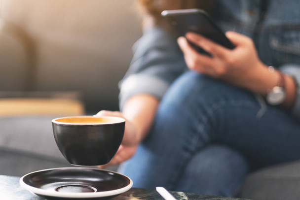 Nahaufnahme einer Frau, die ihr Mobiltelefon hält und benutzt, während sie im Café Kaffee trinkt - Foto, Bild