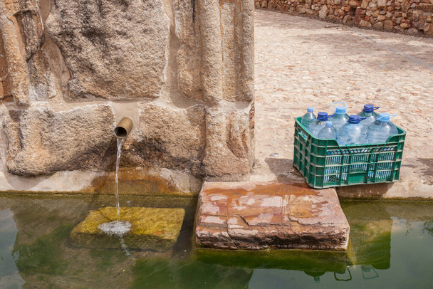Doos vol flessen klaar om te worden gevuld bij Palomas Pillar fontein, Hornachos, Spanje. Keizerlijk wapen van Carlos V in het midden gesneden - Foto, afbeelding