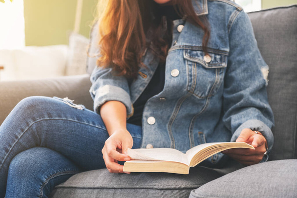 Closeup image of a woman sitting and reading a vintage novel book on sofa - Фото, зображення