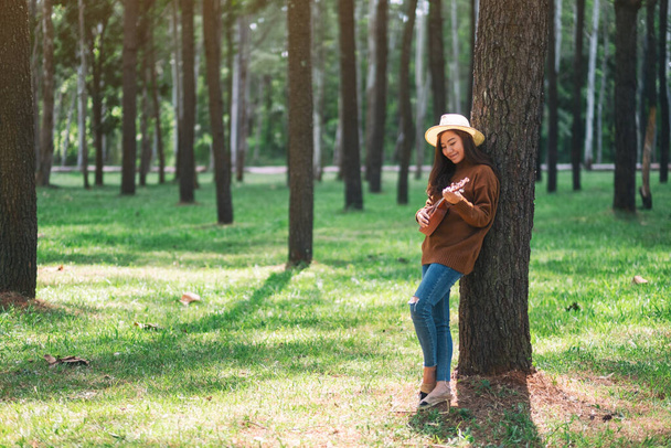 Uma bela mulher asiática de pé e jogando ukulele no parque
 - Foto, Imagem