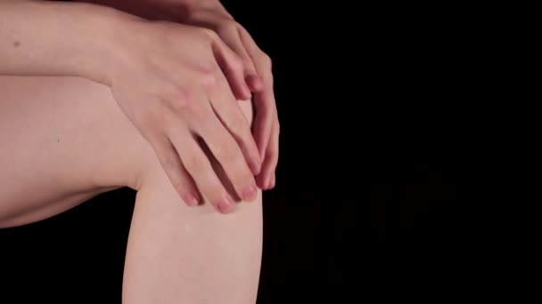 Жінка масажує коліно від болю після травми або операції. Крупним планом ноги на чорному ізольованому фоні в 4K
 - Кадри, відео