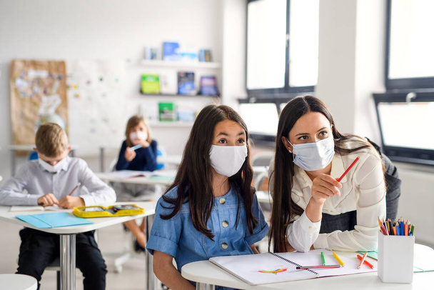 Teacher and children with face mask back at school after covid-19 quarantine and lockdown. - 写真・画像