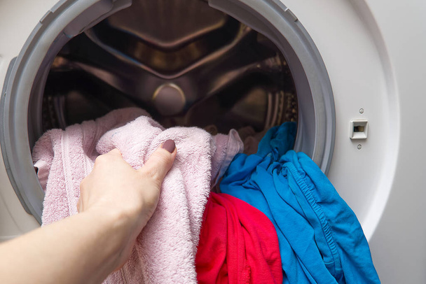 Девушка достает белье из стиральной машины. женщина кладет одежду в стиральную машину
 - Фото, изображение