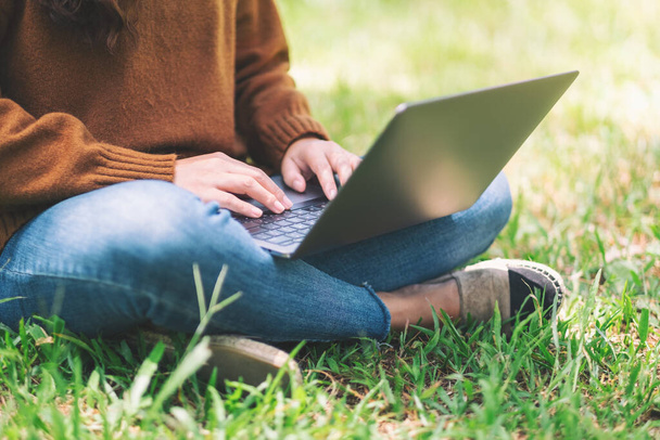 Closeup image of a woman working and typing on laptop keyboard while sitting in the outdoors - Photo, image