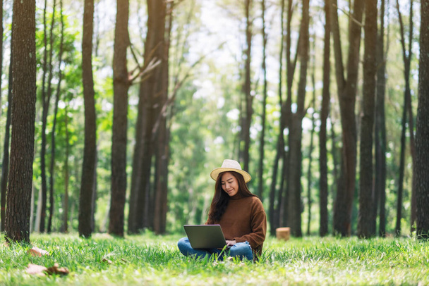 A woman working and typing on laptop keyboard while sitting in the park - Foto, imagen