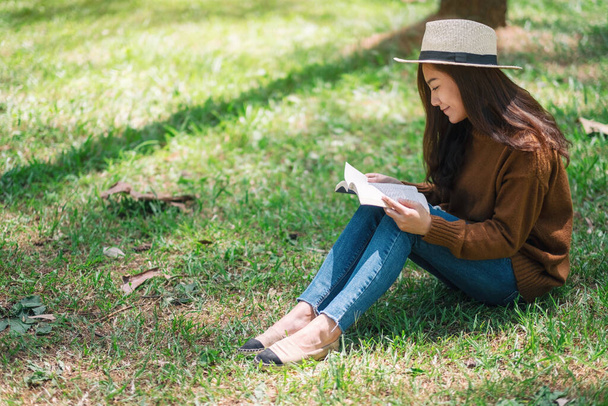 A beautiful Asian woman reading a book while sitting in the park  - Фото, изображение