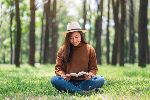 Μια όμορφη Ασιάτισσα διαβάζει ένα βιβλίο ενώ κάθεται στο πάρκο.  - Φωτογραφία, εικόνα