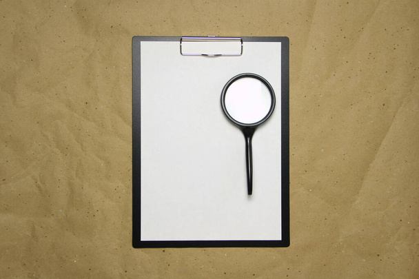 A tablet with a white sheet of A4 format with magnifier on a beige craft paper. Concept of analysis, study, attentive work. Stock photo with empty place for your text and design. - Foto, Bild