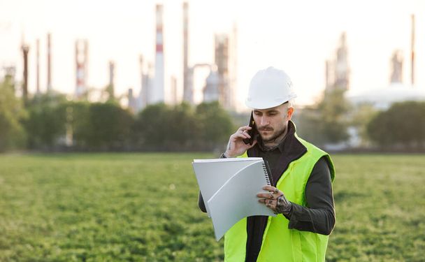 Young engineer with smartphone standing outdoors by oil refinery. Copy space. - Foto, Imagem