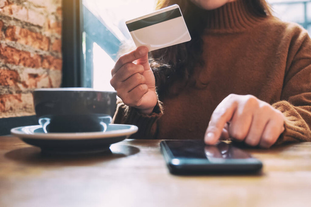 Kobieta trzymająca kartę kredytową i wskazująca na telefon komórkowy do zakupów i zakupów online  - Zdjęcie, obraz