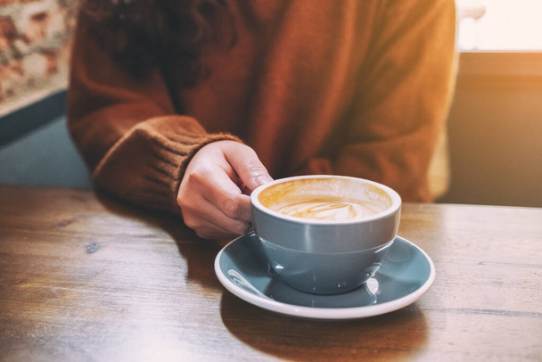 Крупный план женщины, держащей чашку горячего кофе на столе
 - Фото, изображение