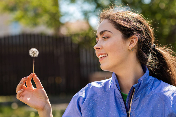 Spring and happiness. Portrait of a Young woman holding a dandelion with a smile. Side view. - Foto, afbeelding