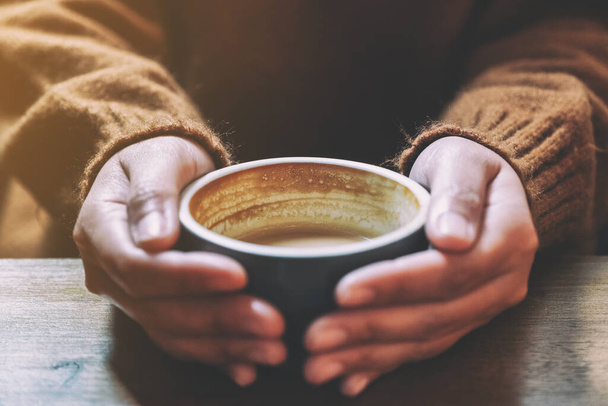 Closeup image of a woman holding a cup of hot coffee on wooden table - Photo, Image