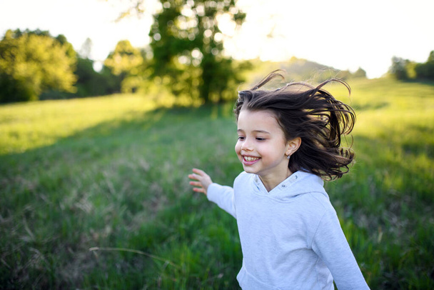 Portrait of small girl running outdoors in spring nature, laughing. - Фото, зображення