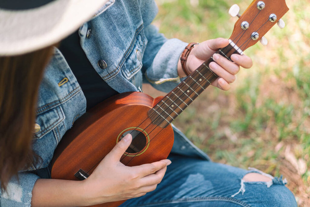 A woman sitting and playing ukulele in the outdoors - Photo, image