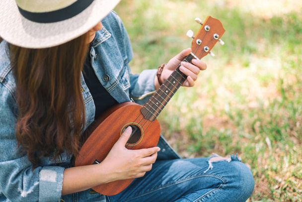 A woman sitting and playing ukulele in the outdoors - Фото, изображение