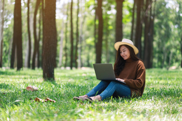 A beautiful asian woman working and typing on laptop keyboard while sitting in the park - Photo, Image