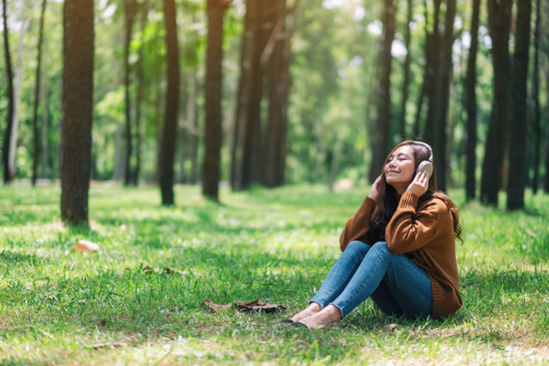 Egy gyönyörű ázsiai nő élvezi hallgatni a zenét fejhallgatóval érzés boldog és nyugodt a parkban - Fotó, kép