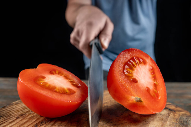 Chef cortando tomate rojo por la mitad con un cuchillo grande en movimiento, poca profundidad de campo, enfoque selectivo, concepto de cocción de verduras
 - Foto, Imagen