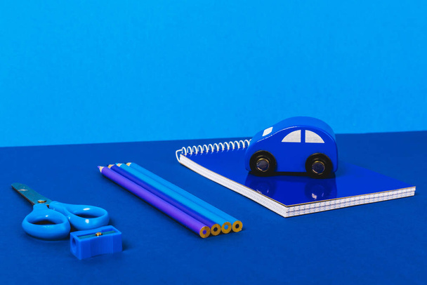 material escolar sobre fondo azul con un coche azul en el cuaderno
 - Foto, imagen