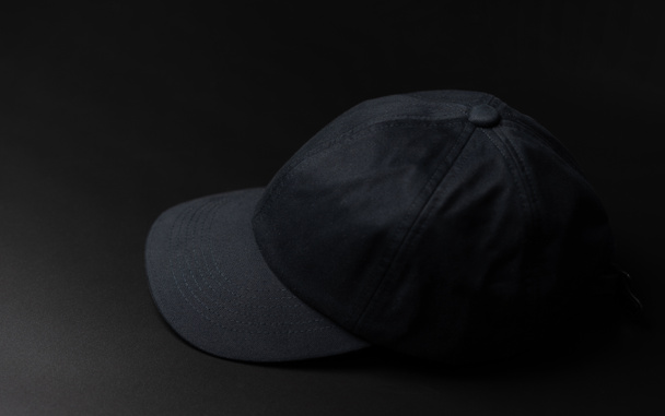 Μαύρο υφασμάτινο καπάκι / καπέλο στο σκούρο μαύρο φόντο. - Φωτογραφία, εικόνα
