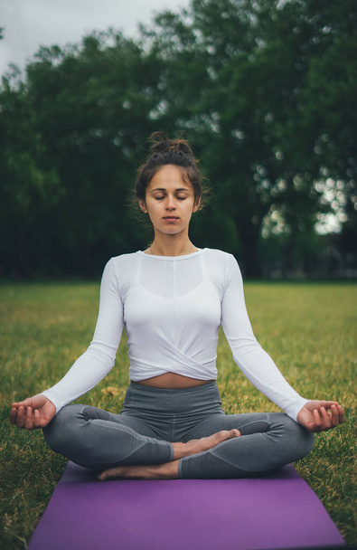 Jovem mulher meditando no parque da manhã verde. Relaxe a pose de ioga. Conceito de ioga e relaxamento
. - Foto, Imagem