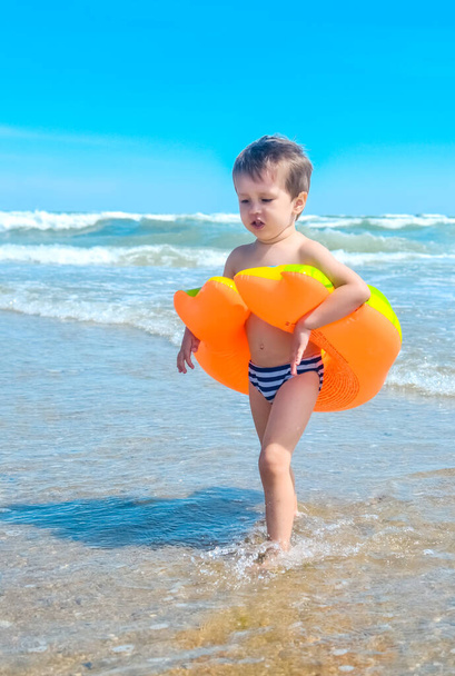 Un petit garçon avec l'anneau de natation marche sur la plage.Un enfant sur une plage tropicale. Amusement au sable et à l'eau, protection solaire pour les petits enfants
. - Photo, image