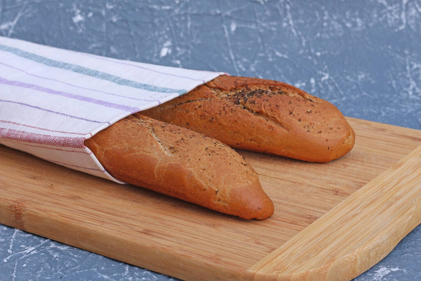 Two fresh french baguettes cools after baking. Bread located on a towel, rustic wooden background. Copy space for text. - Photo, Image