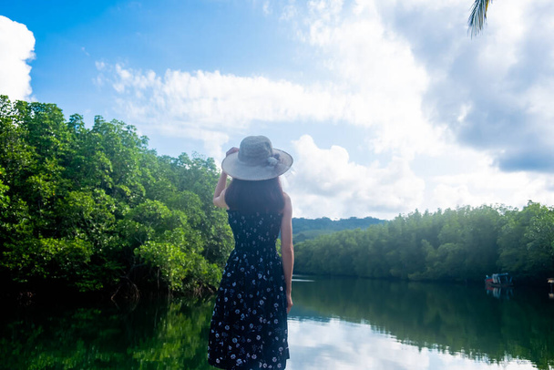 Азійські жінки стоять у капелюсі і милуються видом на річку мангровими лісами. І чисте небо з красивими хмарами. Підходить для туризму, відпочинку і відпочинку. - Фото, зображення