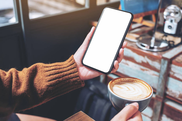 Mockup image of a woman holding black mobile phone with blank desktop screen while drinking coffee in cafe - Foto, Bild