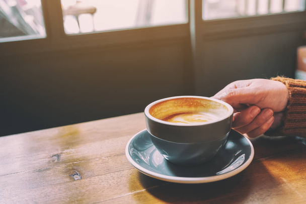 Masanın üzerinde bir fincan sıcak kahve tutan bir elin yakın plan resmi. - Fotoğraf, Görsel