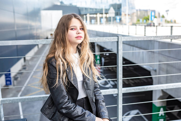 young schoolgirl in black leather jacket posing in the parking lot - Foto, imagen
