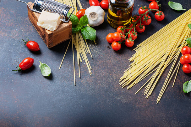 Concept of italian food: spaghetti, tomato, basil, garlic, cheese and olive oil on the black table. Top view with a copy space - Фото, изображение