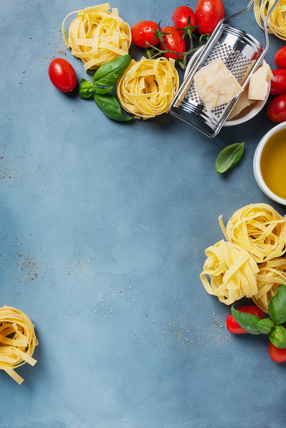Concept of Italian food with raw tagliatelle, tomato, basil, olive oil, salt and pepper on the blue backgraound. Top view image with copy space - Foto, Bild