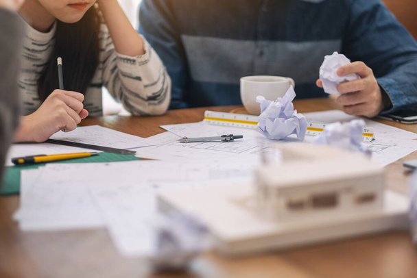 Grupo de un arquitecto se siente estresado después de trabajar en el modelo de arquitectura junto con papel de dibujo tienda en la mesa en la oficina - Foto, imagen