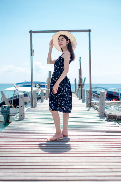 Asian woman tourists go to the sea to stand on the wooden bridge by the beach sand. With beautiful blue sea views Suitable for relaxing on holidays. At Ko Kood, Trat province, Thailand. - 写真・画像