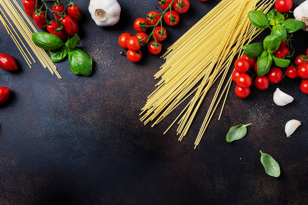 Ingredients for cooking italian pasta: spaghetti, tomato, basil and garlic on the black table. Top view image with a copy space - 写真・画像