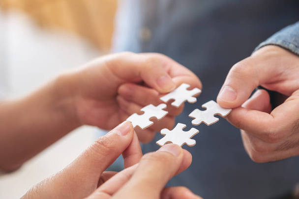 Closeup image of people's hands holding and putting a piece of white jigsaw puzzle together - Photo, Image