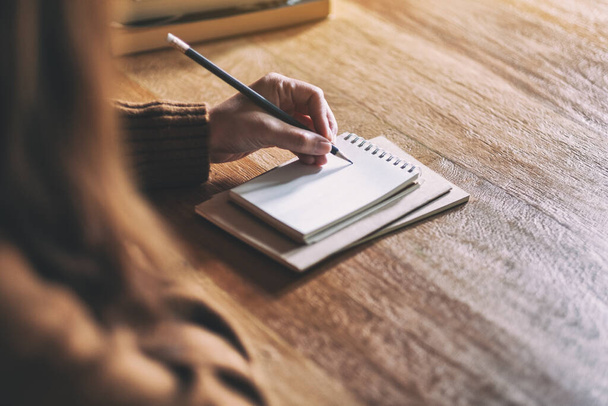 Szoros kép egy nőről, aki üres jegyzetfüzetre ír a fa asztalon. - Fotó, kép