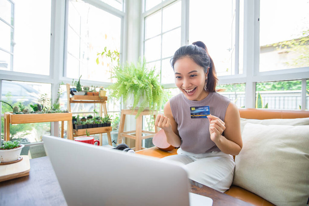Mujer asiática está sosteniendo la tarjeta de crédito y el uso de compras de teléfonos inteligentes en línea en casa. Compras en línea, comercio electrónico, banca por Internet, gasto de dinero, trabajo desde el concepto de casa - Foto, Imagen