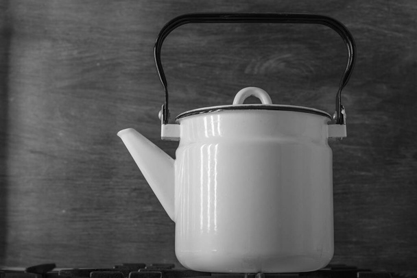 Білий емальований старовинний чайник стоїть на плиті, на чорному тлі крупним планом
 - Фото, зображення