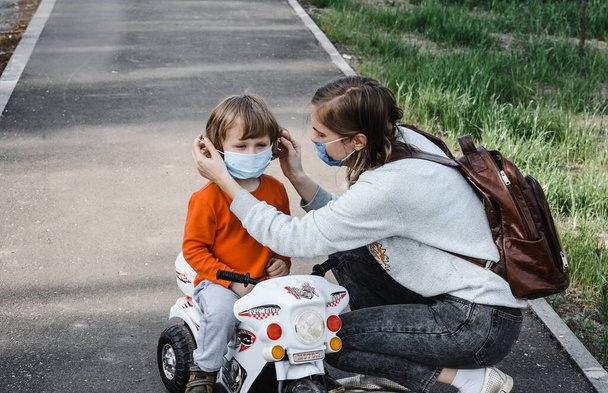 Mam zet een medisch beschermend masker op voor een kind tijdens een wandeling. Bescherming tegen een coronaviruspandemie  - Foto, afbeelding