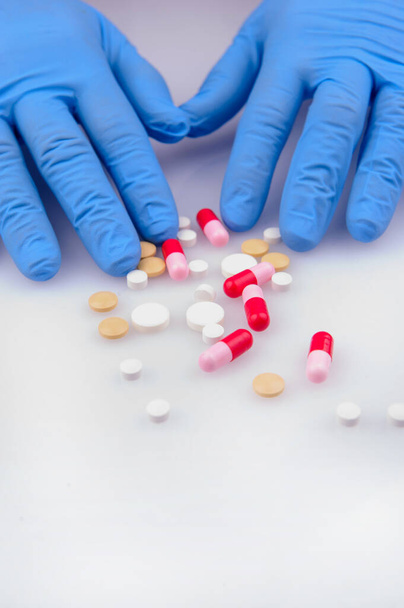 the hands of a doctor in blue gloves holding pills of different color  - Photo, image