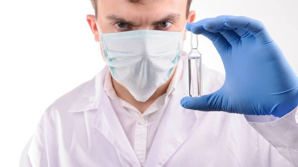 egy fehér egyenruhás orvos nézi az ampullát gyógyszerrel, amit egy kék kesztyűben tart a kezében. - Fotó, kép