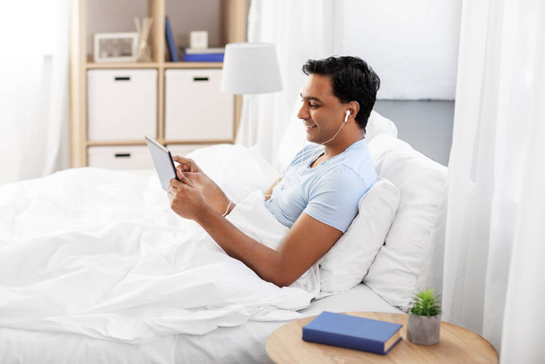 happy indian man with tablet pc in bed at home - Foto, imagen