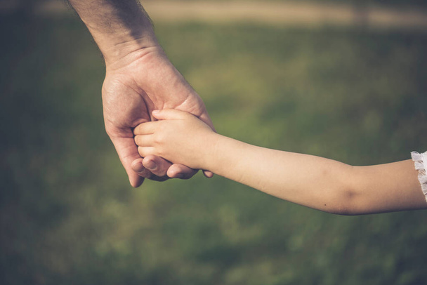 Szülő, aki egy kisgyerek kezét fogja. Apa keze vezeti gyermekét a nyári természetben a szabadban. Családi vagy apák napi koncepció. - Fotó, kép