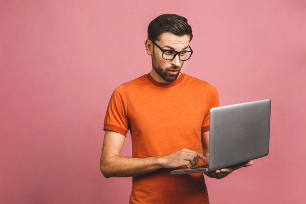 Confident business expert. Confident young amazed handsome man in casual holding laptop and smiling while standing against pink background. - Photo, Image