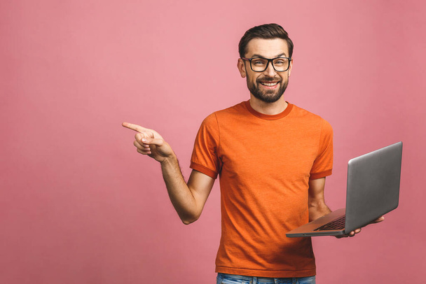 Изображение молодого оптимистичного красивого бородатого мужчины, позирующего изолированно на розовом фоне стены в очках с помощью компьютерного указателя ноутбука, имеют идею
. - Фото, изображение